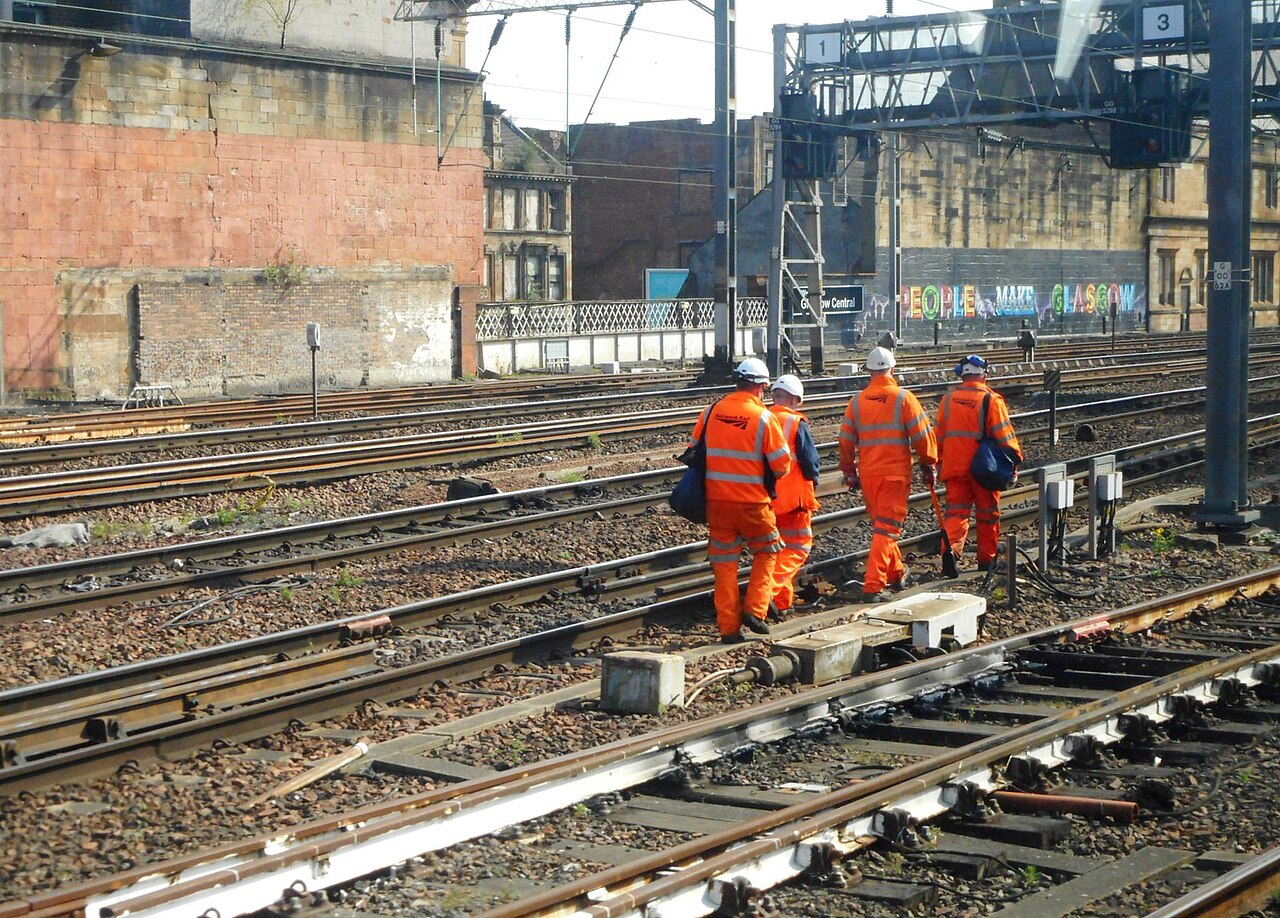 Four railway workers in orange high-visibility clothing walking beside the tracks at Glasgow Central